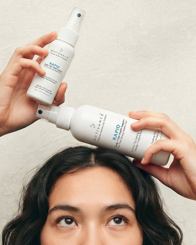 Woman holding two bottles of Activance Rapid scalp and hair growth spray above her dark, wavy hair